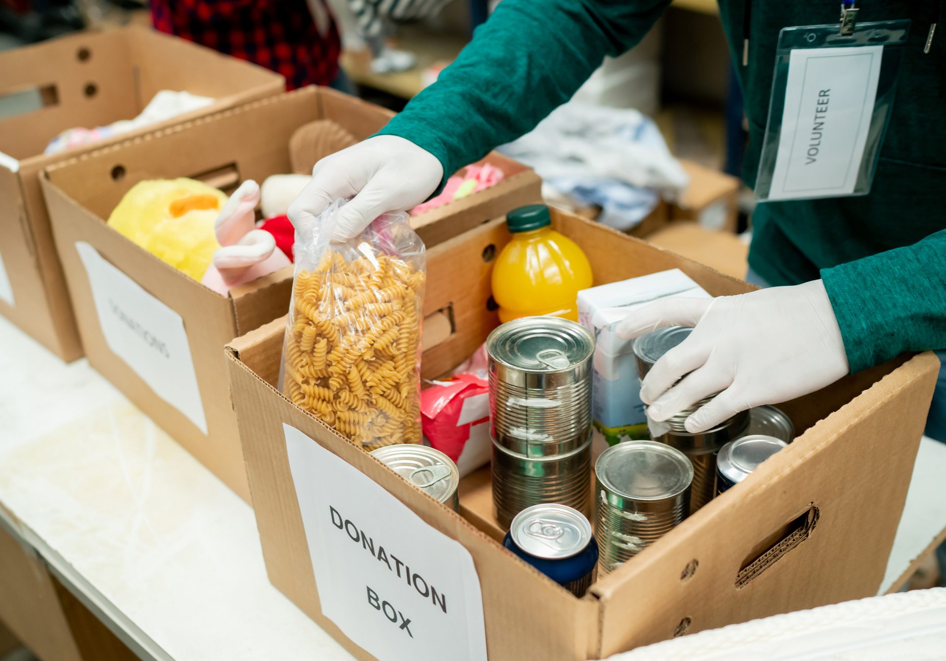 Unrecognizable volunteer organizing donations in boxes wearing protective gloves - Humanitarian aid concepts